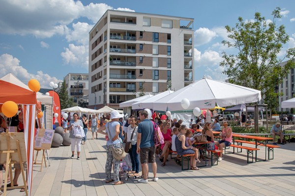 Bei strahlendem Sonnenschein konnten die Besucherinnen und Besucher Livemusik und kulinarische Leckerbissen genießen. (Foto: Buck) Menschen sitzen auf Bierbänken unter Sonnenschirmen, im Hintergrund ein Wohnhaus. (Foto: Buck)