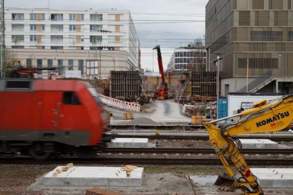 Blick vom Ochsenkopf Richtung Bahnstadt: Hier führt – direkt am Luxor-Kino (rechts) – zukünftig die Gneisenaubrücke über die Bahngleise. (Foto: Stadt Heidelberg) Bild der Baustelle der Gneisenaustraße, während davor ein Zug auf der Strecke fährt.