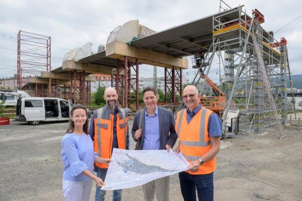 An der Gneisenaubrücke geht es mit riesigen Schritten voran: Die Brücke überspannt nun die Gleise. Die provisorischen Pfosten werden entfernt, sobald der Pylon auf Bergheimer Seite steht. Erster Bürgermeister Jürgen Odszuck (2.v.r.) machte sich mit seinem Team (v.r.) Klaus-Peter Hofbauer (Leiter Tiefbauamt), Christian Hemkendreis (DSK) und Kerstin Maixner (Geschäftsstelle Bahnstadt) ein Bild von den Arbeiten vor Ort. Vier Menschen vor einer Brückenbaustelle