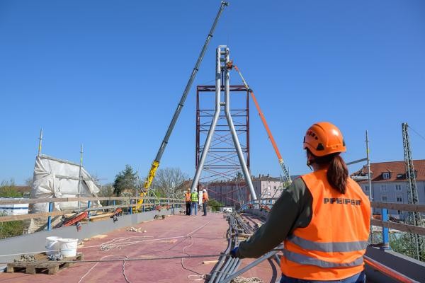Ein Schwerlastkran hebt die Stahlseile zu dem rund 40 Meter hohem Pylon, an dem die Seile befestigt werden. (Foto: Rothe) Eine Person blickt zu einem Pylon auf einer Brücke