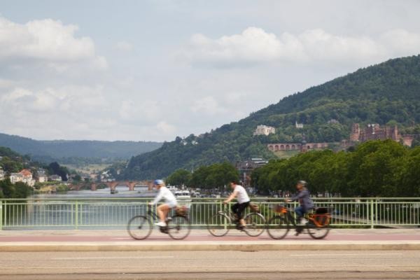 Fahrradstadt Heidelberg: Bereits heute werden 38 Prozent aller Wege im Stadtgebiet mit dem Rad zurückgelegt. (Foto: Stadt Heidelberg) Drei Fahrradfahrerinnen und Fahrradfahrer fahren über eine Brücke in Heidelberg. Im Hintergrund sieht man die Alte Brücke und das Heidelberger Schloss.