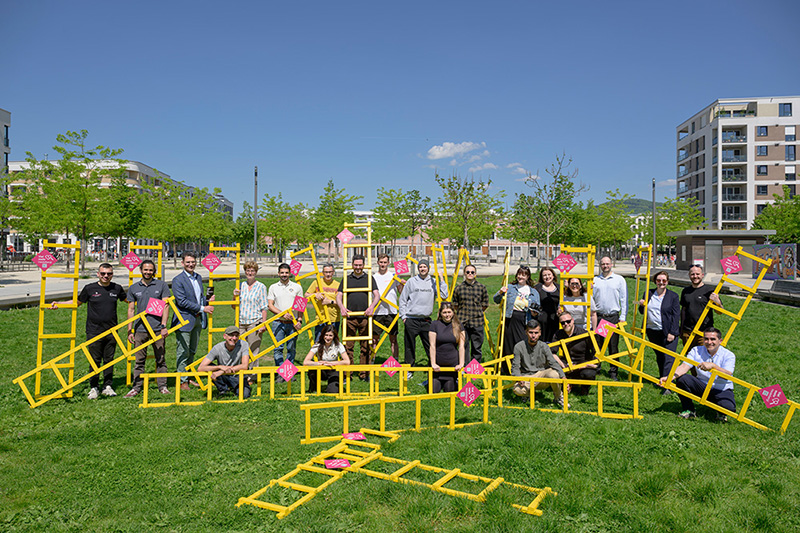 Größere Menschengruppe posiert mit einigen gelben Leitern auf einer grünen Wiese.