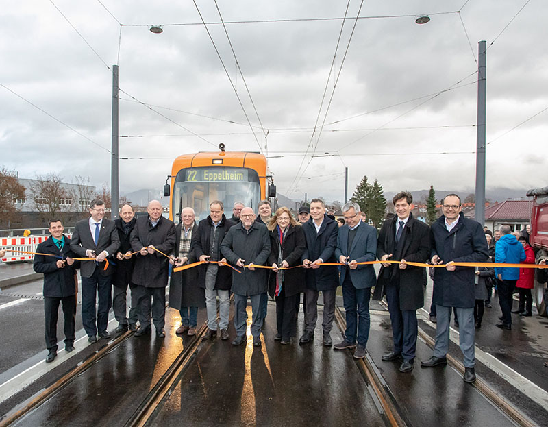 Viele Menschen haben sich vor einer Straßenbahn auf den Gleisen versammelt, um gemeinsam ein orangenes Band zu zerschneiden. (Foto: Nikola Haubner)