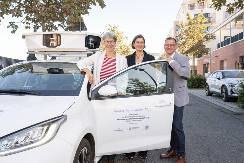 Raoul Schmidt-Lamontain, Martina Pfister und Elke Zimmer stehen in der geöffneten Tür des weißen Scan-Fahrzeuges.